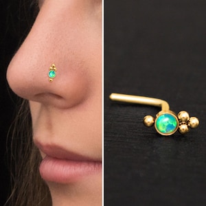 May include: Gold nose ring with a green opal gemstone and small gold beads. The ring is curved to fit the nose.