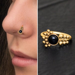 Puede incluir: Anillo de nariz de oro con una piedra preciosa negra y un diseño de cuentas.