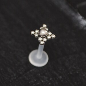 May include: Silver body jewelry with a clear acrylic post and a square-shaped top with a cluster of small silver balls.