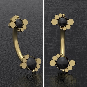 May include: Gold body jewelry with a curved barbell and black gem accents. The barbell is adorned with multiple small round gems on each end.