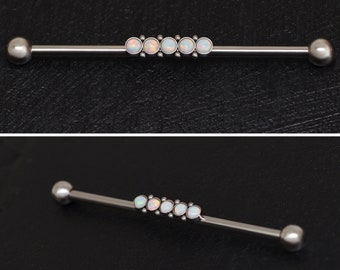 Puede incluir: Una barra de plata con cinco piedras de ópalo blancas. La barra es una joya de piercing corporal.