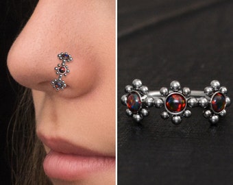 May include: A silver nose ring with three opal flower charms. The ring is shown on a person's nose and also laid flat on a black surface.
