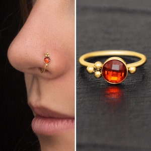 May include: Gold nose ring with a red gemstone and three small gold beads.