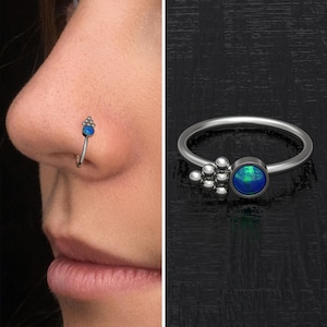 Può includere: Un anello per il naso in argento con un gruppo di piccole perle e una pietra preziosa di opale blu.