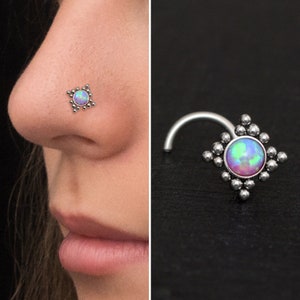 Può includere: Un anello per il naso in argento con un piccolo opale iridiscente rotondo incastonato in una cornice quadrata con piccole perle attorno al bordo.