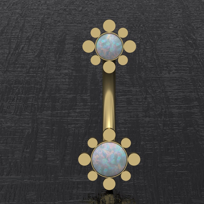 May include: Gold body jewelry with two opal gemstones set in a circular design with smaller gold circles surrounding each stone.
