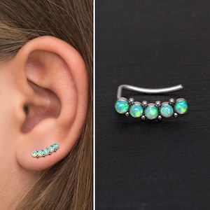 May include: A silver ear cuff with five green opal stones. The cuff is curved and has a small bead between each stone.