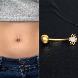 Puede incluir: Anillo de ombligo dorado con una piedra de ópalo transparente y una bola dorada en el otro extremo.