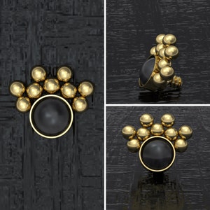 May include: A gold body jewelry piece with a black gem and a cluster of small gold balls around it.