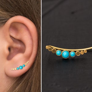 Puede incluir: Pendiente de oreja de oro con un diseño curvo y piedras turquesa. El pendiente se lleva en la parte superior de la oreja.