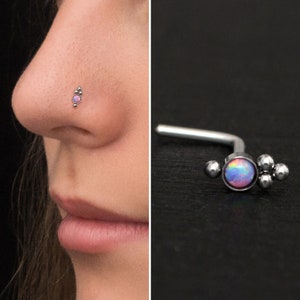 Op de afbeelding: Een zilveren neusring met een kleine, ronde, iriserende opaal-edelsteen en drie kleine zilveren kralen. De neusring is te zien op de neus van een model.