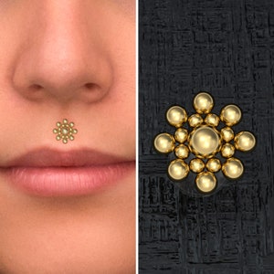 May include: Gold lip piercing with a cluster of small round beads in a flower shape.