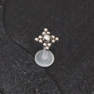 May include: Silver body jewelry with a clear acrylic post and a silver star-shaped top with a central round bead.