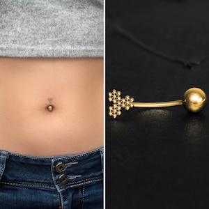 Puede incluir: Anillo de ombligo dorado con una pequeña bola en un extremo y un diseño en forma de corazón en el otro extremo.