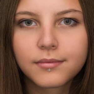 May include: Close-up portrait of a person with long brown hair. The person has a small silver stud piercing below their lower lip.