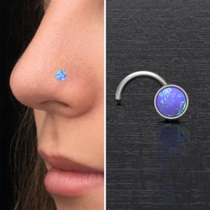 Peut inclure: Un anneau de nez en argent avec une pierre précieuse en opale bleue. L'anneau est incurvé et se termine par une petite boule. L'opale est irisée et présente une variété de couleurs.
