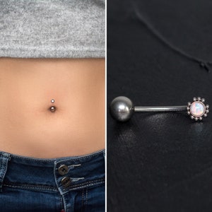 Puede incluir: Un piercing de ombligo plateado con una pequeña gema transparente. El piercing se muestra en el ombligo de una persona. Una imagen separada muestra un piercing de ombligo plateado con una gema de ópalo rosa más grande.