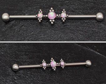 Puede incluir: Una barra de plata con tres piedras de ópalo rosa engastadas en un diseño decorativo. La barra es una joya de piercing corporal.