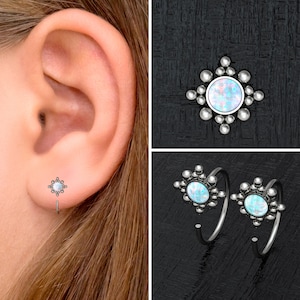 May include: A pair of silver hoop earrings with a small opal gemstone in the center of each hoop. The hoops are decorated with small silver beads around the gemstone.