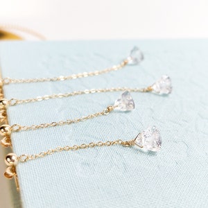 Könnte beinhalten: Drei goldene Ketten mit klaren Kristallanhängern, die von einer blauen Oberfläche hängen. Die Ketten sind unterschiedlich lang und die Kristalle haben unterschiedliche Größen.