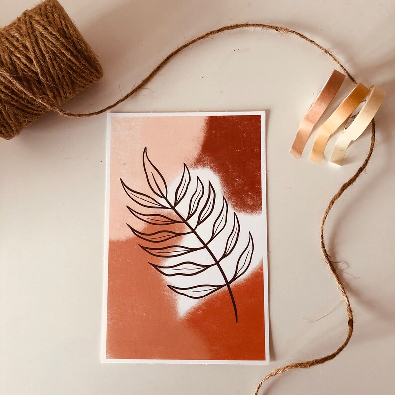 May include: A minimalist art print featuring a stylized leaf in black against a background of abstract brown, orange, and pink watercolor washes.