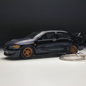 May include: Black die-cast model car keychain of a Mitsubishi Lancer Evolution. The car has gold wheels and a silver keychain.