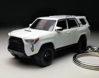 Puede incluir: Llavero Toyota 4Runner blanco con parrilla negra y ruedas negras. El llavero está hecho de metal y tiene un anillo plateado.