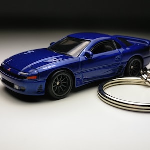 Op de afbeelding: Een blauwe, gegoten model auto sleutelhanger van een Mitsubishi 3000GT. De auto is een tweedeurs coupé met een zilveren sleutelring.