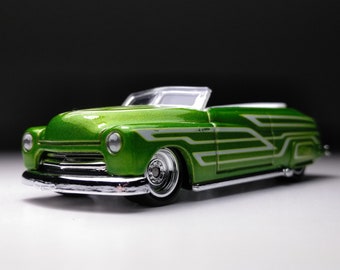 May include: A green and white custom-painted toy car model with a convertible top. The car has a chrome bumper and white pinstripes.
