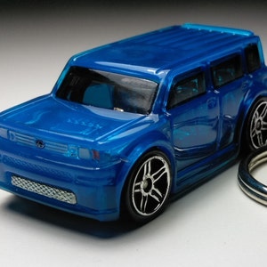 May include: A blue plastic toy car keychain of a Toyota Scion xB. The car has black wheels and a silver grille.