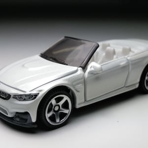 May include: A white toy convertible car with black wheels and a black windscreen frame. The car has a sleek design with visible interior details. The car is a miniature replica of a BMW M4.