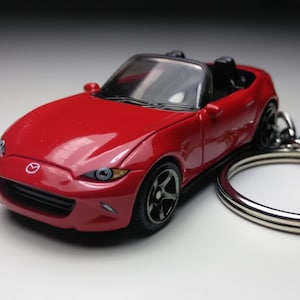May include: A red Mazda MX-5 Miata convertible keyring. The keyring is made of metal and features a detailed design of the car.