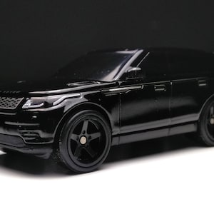 May include: A black toy car model of a Range Rover Velar SUV. The car has black wheels and a detailed front grille.