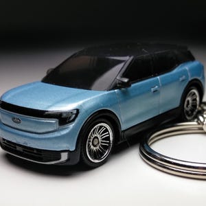 Op de afbeelding: Een modelauto van een lichtblauwe SUV met een zwart dak. De miniatuurauto heeft gedetailleerde wielen en een Ford-logo. Een zilveren sleutelhanger is bevestigd. De auto is ongeveer 10 cm lang.