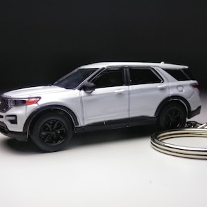 Puede incluir: Un modelo de SUV plateado con ruedas y molduras negras, presentado como llavero. El vehículo en miniatura tiene un diseño detallado, incluyendo una parrilla delantera y faros. Un llavero plateado está adjunto.
