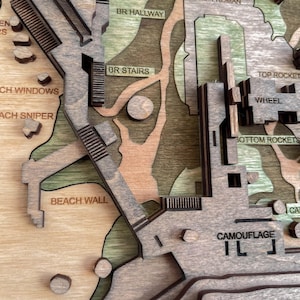 May include: A detailed wooden map with layered construction, featuring text labels like "BR WINDOW" and "CAMOUFLAGE." The map incorporates various shades of brown and green, with architectural elements and terrain features. The design includes stairs, walls, and other structures.