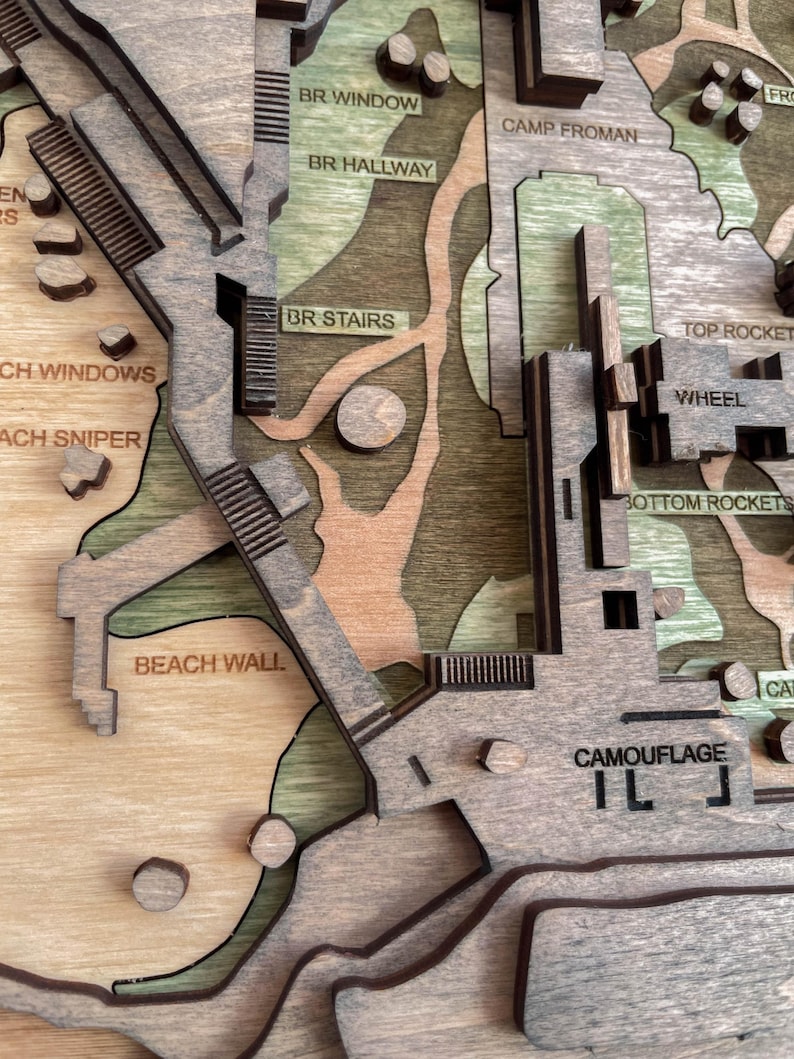 May include: A detailed wooden map with layered construction, featuring text labels like "BR WINDOW" and "CAMOUFLAGE." The map incorporates various shades of brown and green, with architectural elements and terrain features. The design includes stairs, walls, and other structures.
