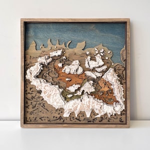 Puede incluir: Un mapa topográfico 3D enmarcado. El mapa presenta cortes de madera en capas en tonos marrón, naranja, verde y blanco, que representan formaciones terrestres. El fondo es azul y el marco es de color marrón claro.