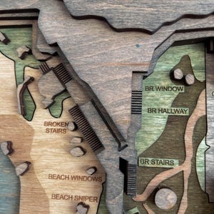 May include: A multi-layered wooden map with various sections labeled. The map features text labels such as "BROKEN STAIRS", "BEACH WINDOWS", and "BR STAIRS". The color palette includes shades of brown, green, and gray.