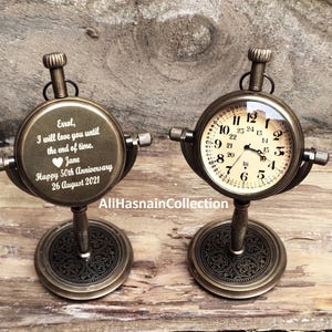 Peut inclure: Deux horloges de style compas antique avec un support décoratif. Le cadran de l'horloge de gauche porte un message personnalisé : "Eval, je t'aimerai jusqu'à la fin des temps. Jane Joyeux 50e anniversaire 26 août 2021".