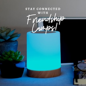 May include: A blue and white Friendship Lamp with the text "Stay Connected with Friendship Lamps!" on a white background. The lamp is on a wooden table with a laptop and other items.