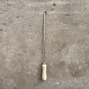 Peut inclure: Un long outil crochet en métal fin doté d'un manche en bois clair et lisse à une extrémité. La tige est droite et fine, se terminant par un petit crochet courbé au sommet, conçu pour des tâches de manipulation ou de traction manuelle.