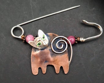 May include: A copper cat brooch with a silver swirl tail and green eyes. The cat is attached to a silver safety pin with pink beads.