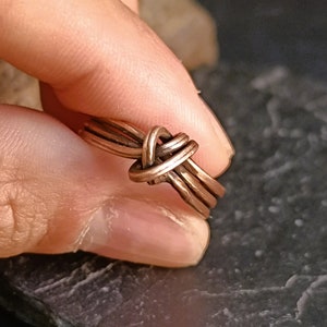 May include: A copper wire ring with a knot design. The ring is made of multiple strands of wire that are twisted together to create a knot.