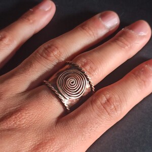 Könnte beinhalten: Ein Kupferring mit einem Spiraldesign. Der Ring wird an einem Finger getragen.