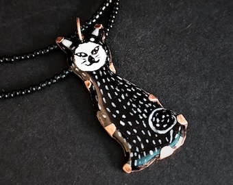 May include: Black and white ceramic cat pendant necklace with a copper chain. The cat has a white face with black eyes and a black body with white spots.