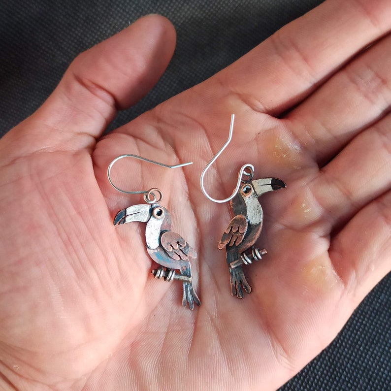 May include: A pair of toucan bird earrings with silver hooks and a copper and white painted finish.