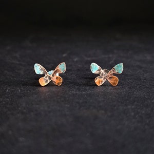 Op de afbeelding: Een paar kleine vlindervormige oorbellen met een gehamerde textuur. De oorbellen zijn een mix van turquoise en koperkleuren.