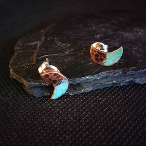 Peut inclure: Une paire de boucles d'oreilles en forme de croissant de lune en argent et en cuivre avec une texture martelée et une patine bleu turquoise.