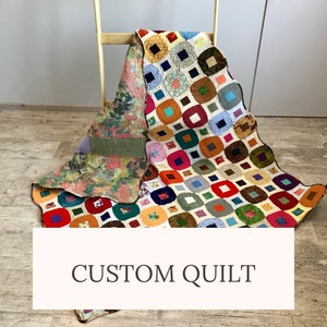 May include: A colorful custom quilt draped over a wooden chair. The quilt features a patchwork design with squares of various colors, including red, blue, orange, and green. The reverse side displays a floral pattern. The text "CUSTOM QUILT" is visible.